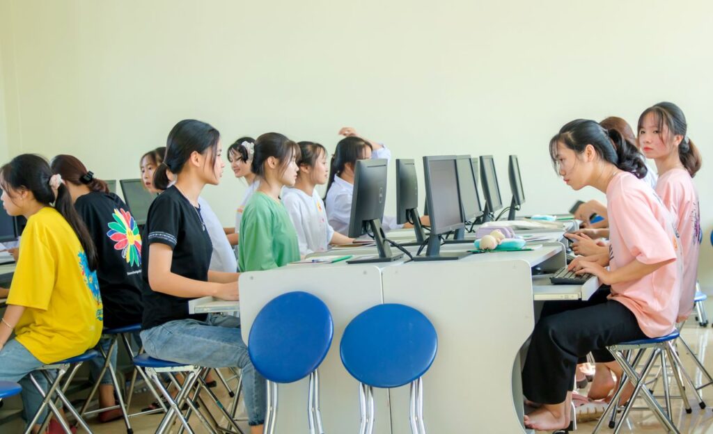 Students in a computer lab working together on computers, showcasing teamwork and education. Computer Shop