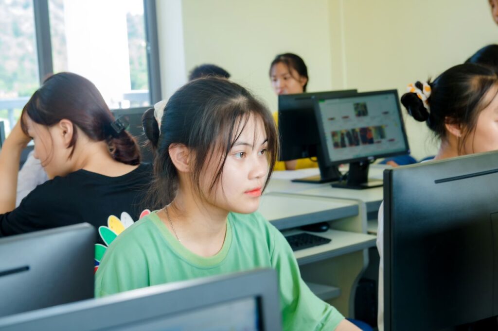 Asian students focused on studying technology in a bright computer classroom setting.